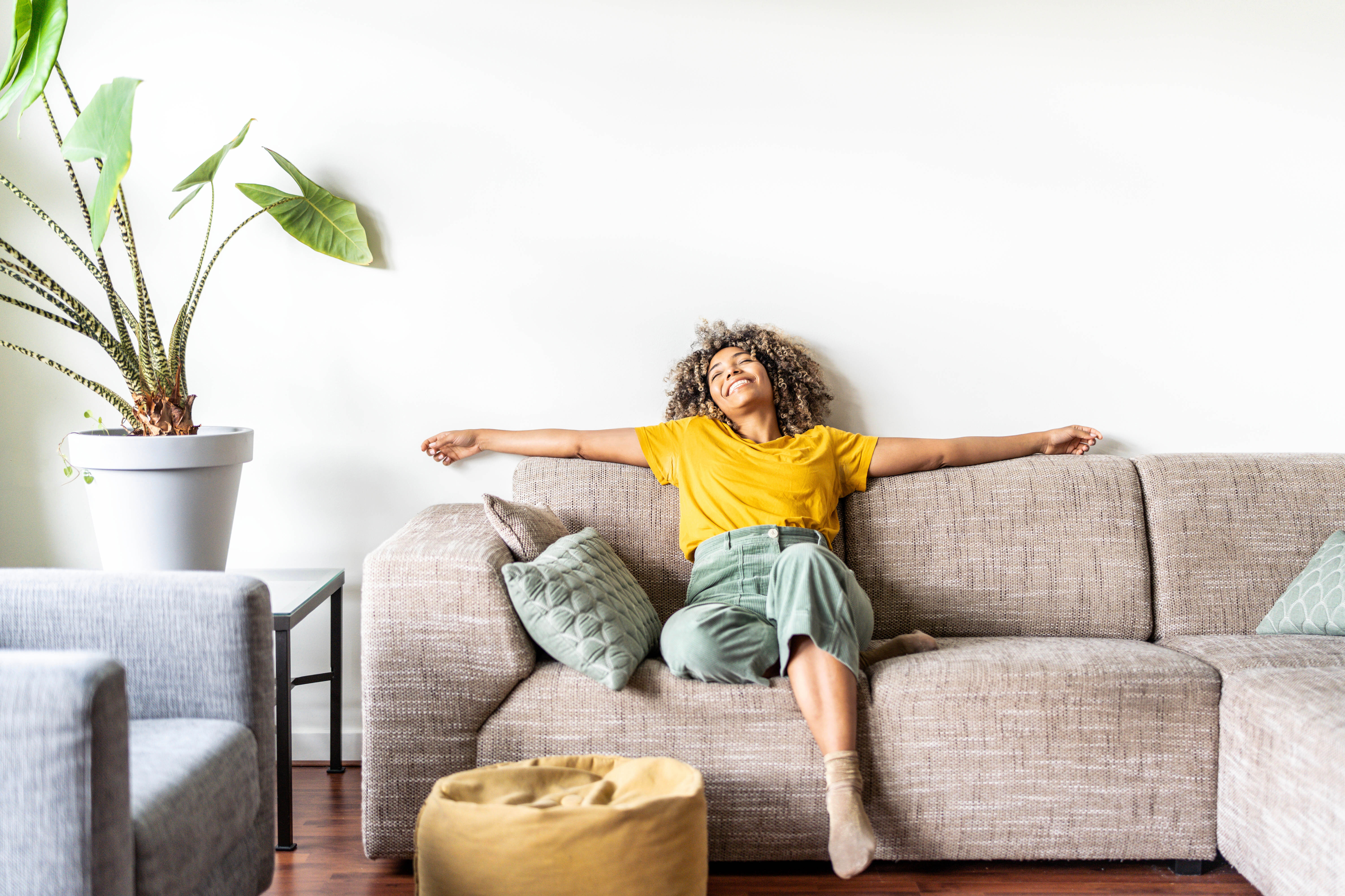 Gesundes Wohnen - Frau sitzt glücklich auf einem Sofa